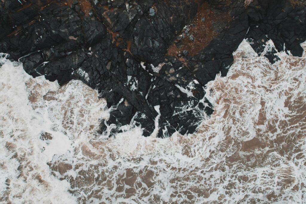 Aerial shot of waves crashing on black rocks at the coast of Karwar, India.