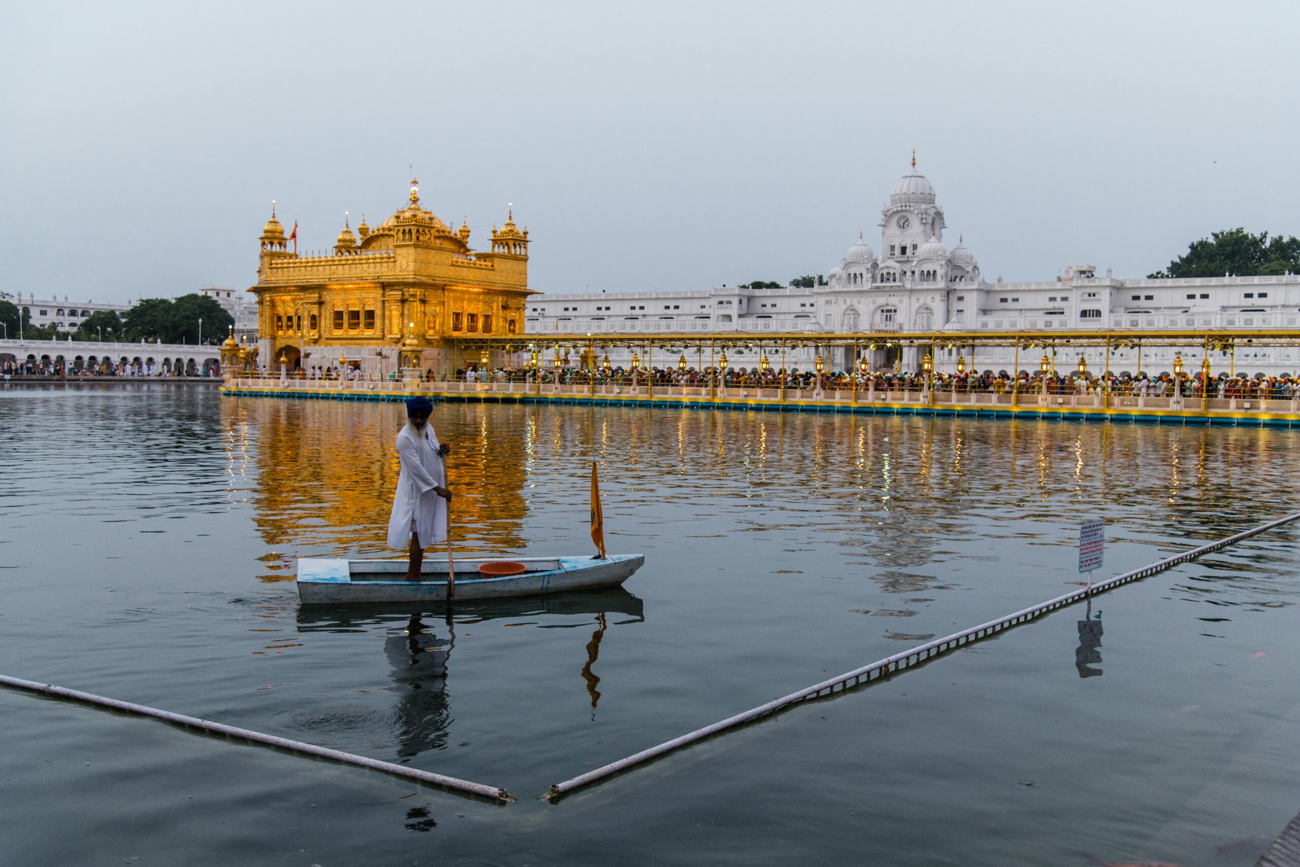 Sikh man on boat in front of the illuminated Golden Temple in Amritsar.