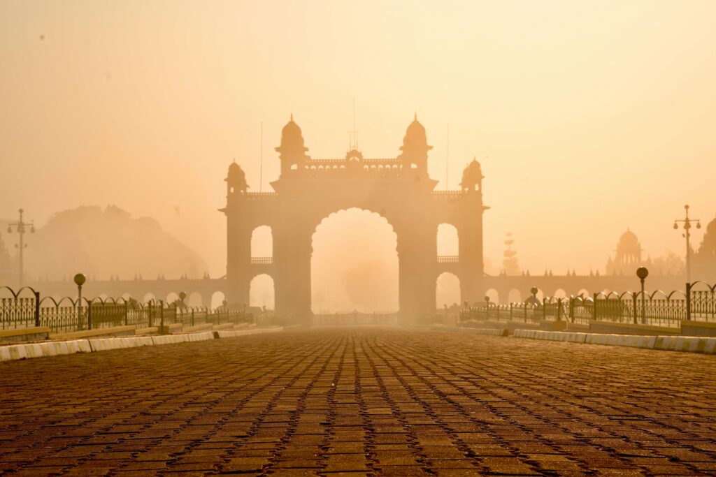 The Mysore Palace gate stands majestically enveloped in a golden morning fog, showcasing elegant 18th-century architecture.