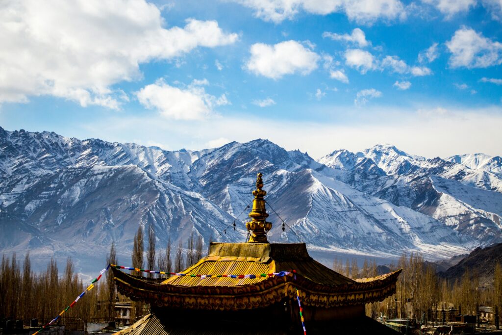 Stunning landscape of Leh's mountain range and traditional temple roof under a blue sky.